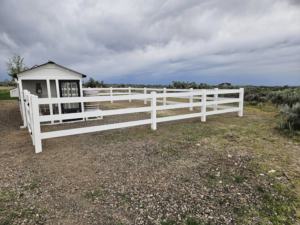 A white vinyl paddock-style fence enclosing an area next to a small shed, installed by Regan Fencing & Services in Nampa, ID.