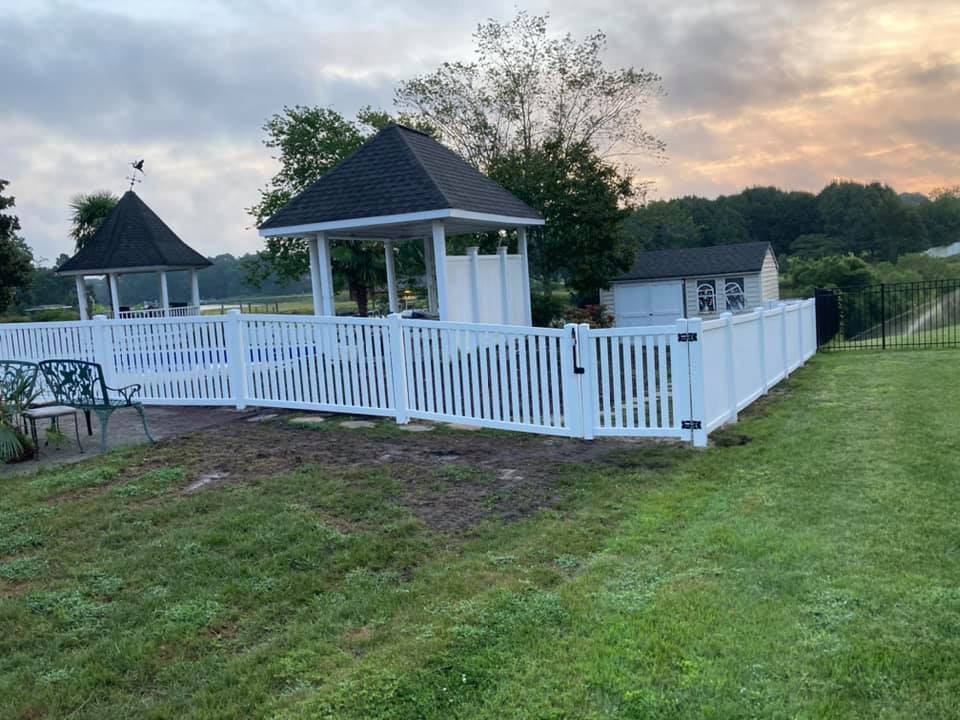 A white vinyl picket fence enclosing a gazebo and shed by Sea Level Fence in Harbinger, NC