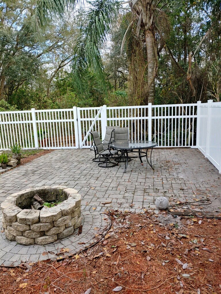 A white vinyl picket fence enclosing a paved patio with a fire pit, installed by Big Jerry's Fencing of Boise ID in Holly Springs, NC.