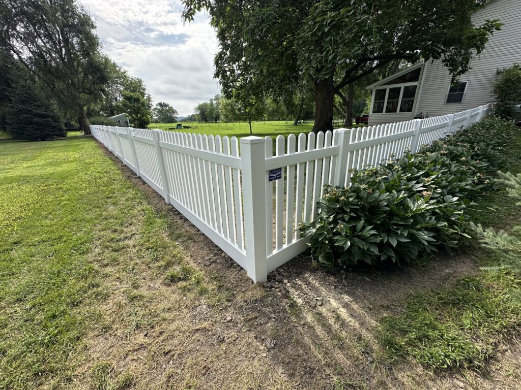 A white vinyl picket fence installed in a residential yard by Bostwick Fencing, LLC in Sioux City, IA.