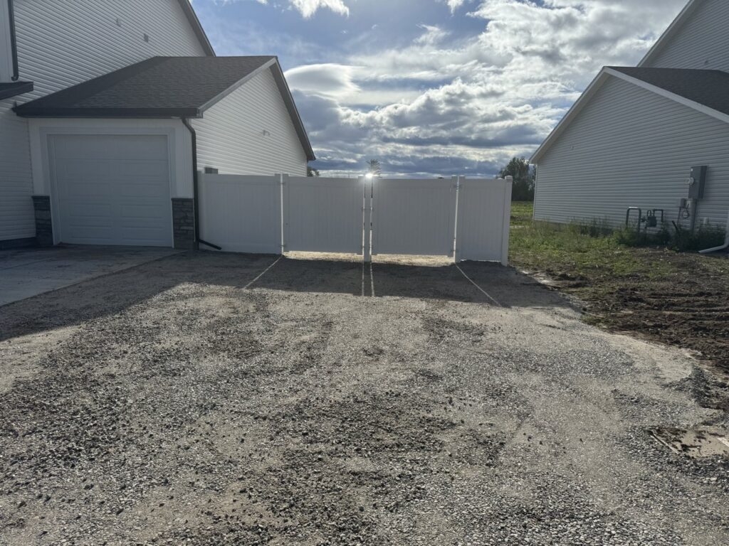 A white vinyl privacy double gate installed by 208 Fence and Gate, separating a gravel area in Idaho Falls, ID.