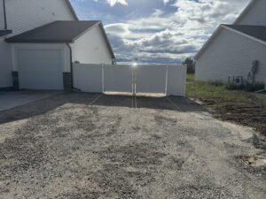 A white vinyl privacy double gate installed by 208 Fence and Gate, separating a gravel area in Idaho Falls, ID.