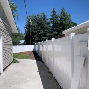 A white vinyl privacy fence installed along the side of a residential house and pathway by Performance Fencing in Rigby, ID.