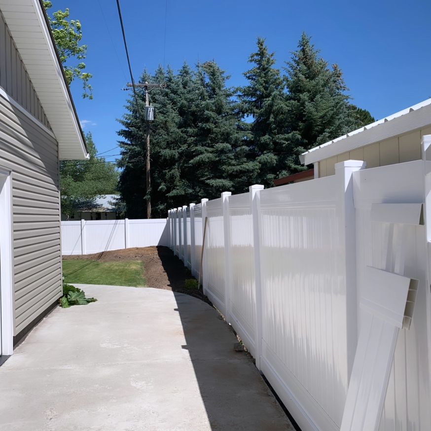 A white vinyl privacy fence installed along the side of a residential house and pathway by Performance Fencing in Rigby, ID.