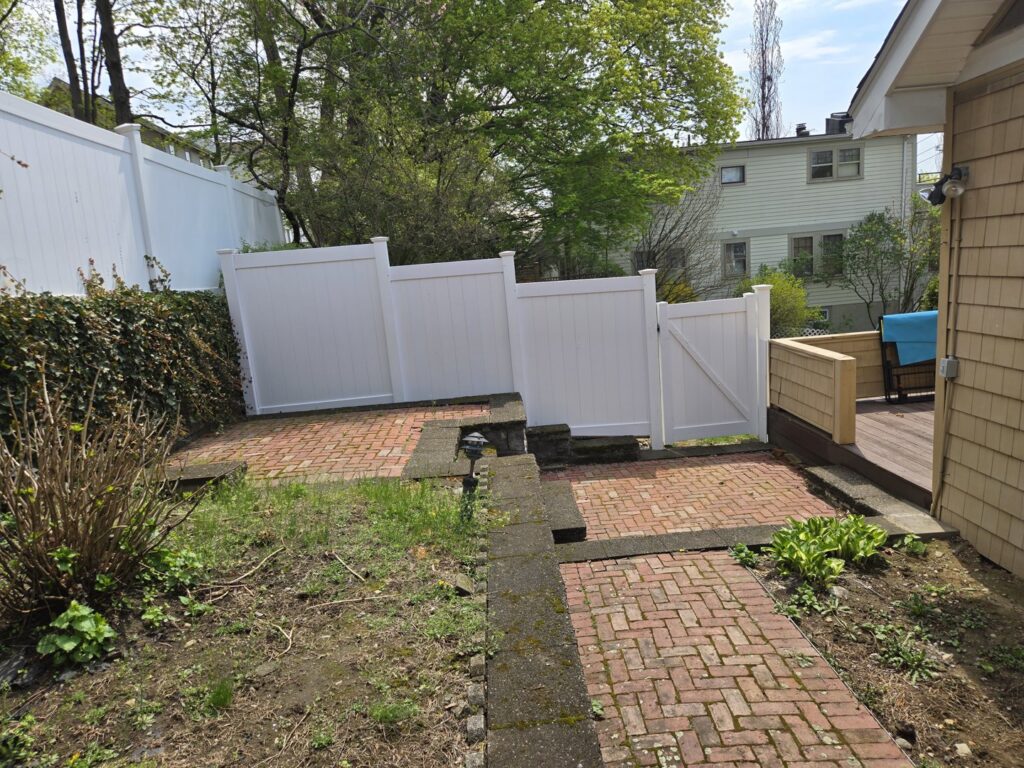 A white vinyl privacy fence with a gate installed next to a brick patio by Matul Fence Inc in Lynn, MA