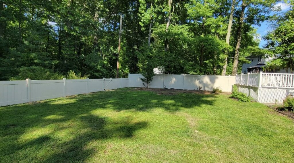 A newly installed white vinyl privacy fence with a gate in a residential backyard by Concord Fence Llc in Wilmington, DE