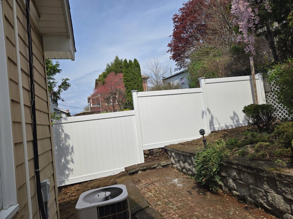 A white vinyl privacy fence installed in a backyard next to an AC unit by Matul Fence Inc in Lynn, MA