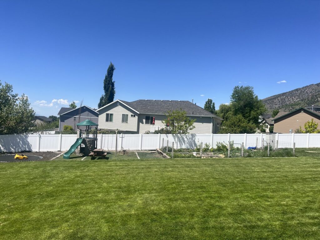 A white vinyl privacy fence installed in a backyard with a playground by Sublime Fencing LLC in North Logan, UT.