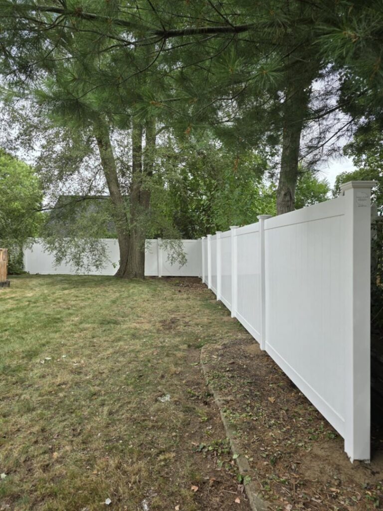 A tall white vinyl privacy fence providing seclusion in a backyard by Precision Fence NH in Hooksett, NH.