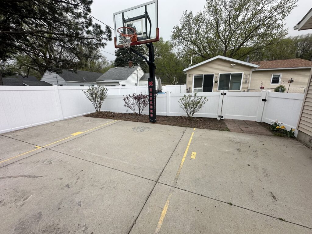 A white vinyl privacy fence enclosing a residential basketball court by Bostwick Fencing, LLC in Sioux City, IA.