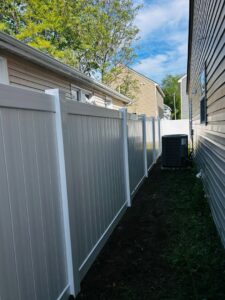A newly installed white vinyl privacy fence running between two residential homes by Fast Fences LLC in Northfolk, VA.