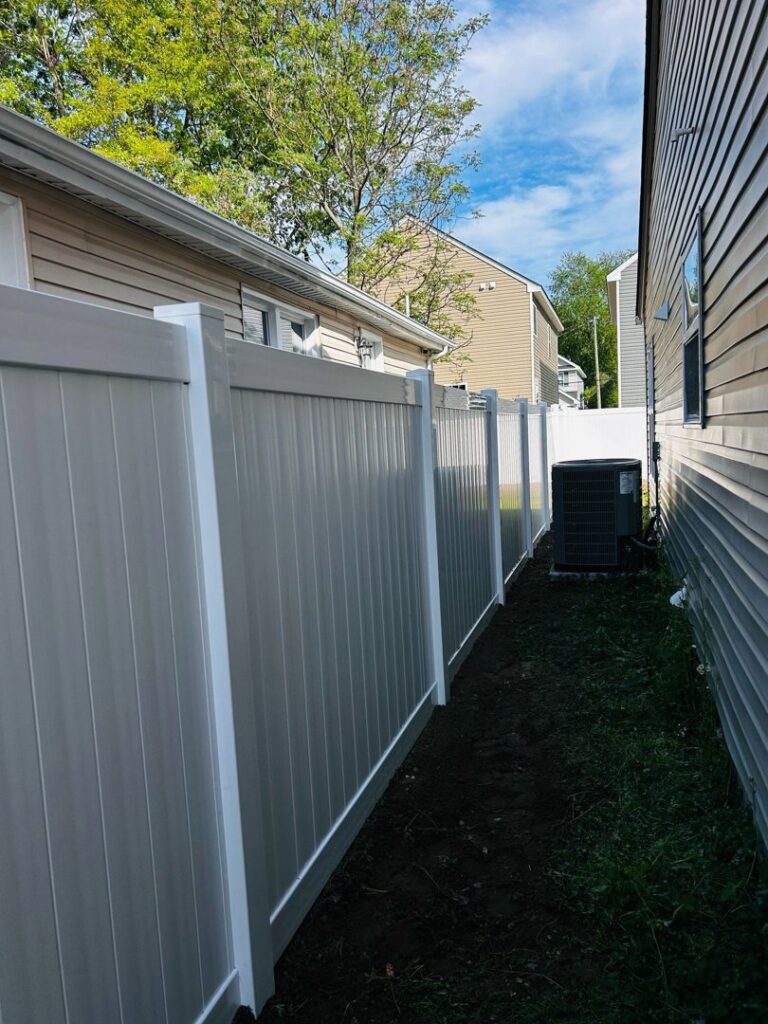 A newly installed white vinyl privacy fence running between two residential homes by Fast Fences LLC in Northfolk, VA.