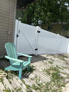 A white vinyl privacy fence with a gate installed next to a wooden deck by Schumacher Fencing, LLC in Columbus, NE.