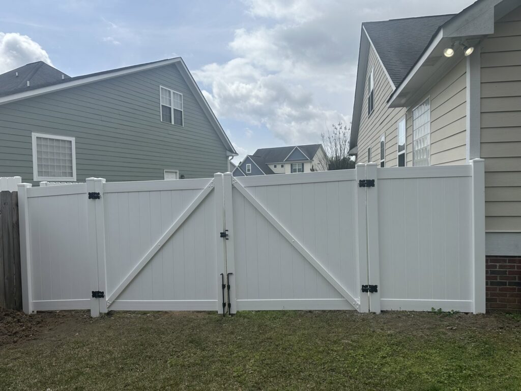 A white vinyl privacy fence with a double gate installed in a residential backyard by Fayetteville Fence Pros in Fayetteville, NC.