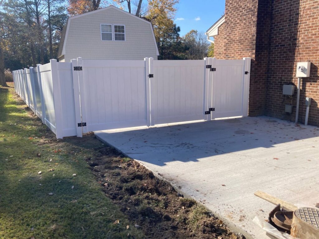 A white vinyl privacy fence with a double gate next to a concrete pad by Sea Level Fence in Harbinger, NC
