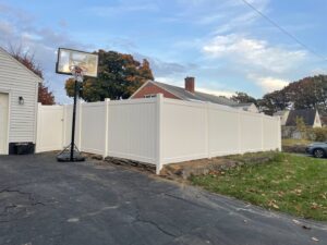 A newly installed white vinyl privacy fence along a residential driveway by Vision One Construction in Schenectady, NY