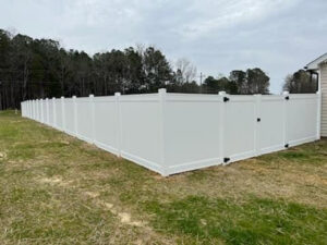 A long white vinyl privacy fence with a gate installed around a property by Fencingphd.nc in Fayetteville, NC.
