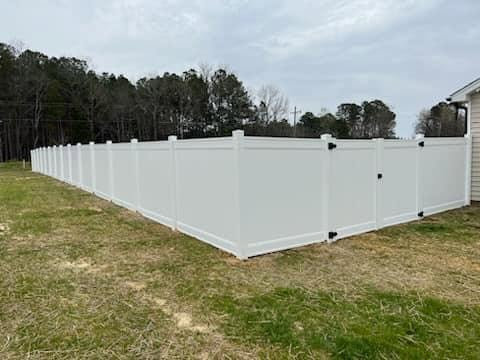 A long white vinyl privacy fence with a gate installed around a property by Fencingphd.nc in Fayetteville, NC.