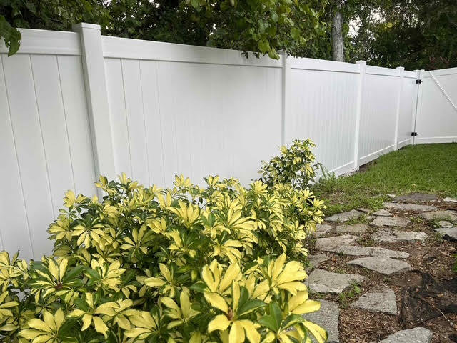 A pristine white vinyl privacy fence bordering a garden area, installed by Native Outdoors, LLC in Orlando, FL.