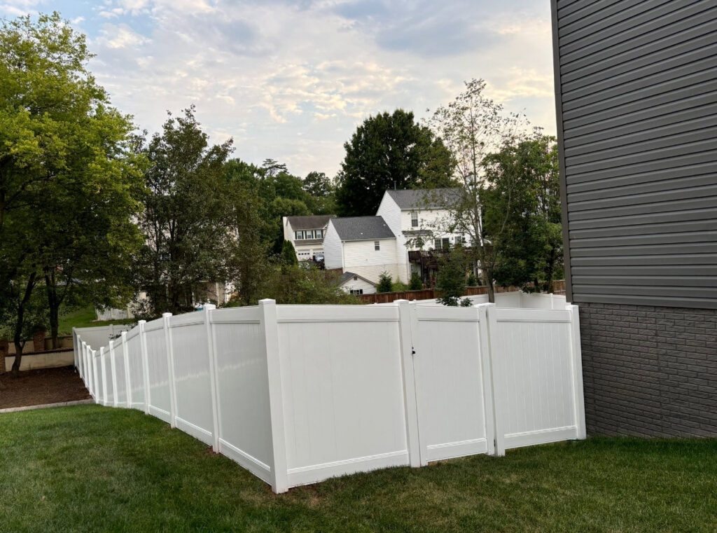 A white vinyl privacy fence with a gate installed in a residential backyard by Universal Fence LLC in Drainesville, VA.
