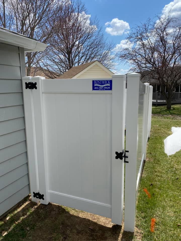 A white vinyl privacy fence gate installed next to a residential home by Bostwick Fencing, LLC in Sioux City, IA.
