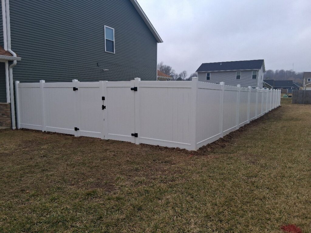 A long white vinyl privacy fence with a gate installed in a residential backyard by Morton Fence Solutions LLC in Indianapolis, IN.