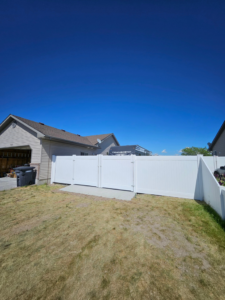 A newly installed white vinyl privacy fence with a double gate in a residential backyard by Performance Fencing in Rigby, ID.
