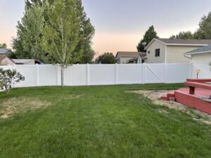 A white vinyl privacy fence with a gate installed in a residential backyard by All American Vinyl in Provo, UT.