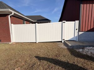 A white vinyl privacy fence with a gate connecting two buildings, installed by Shatkoff Fencing in Louisville, KY.