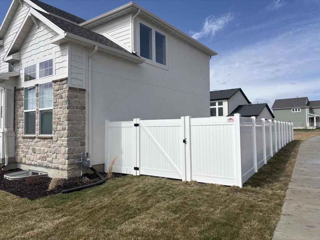 A white vinyl privacy fence with a gate installed in a side yard by Sublime Fencing LLC in North Logan, UT.