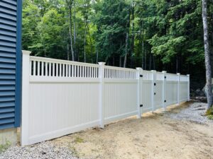 A white vinyl privacy fence with a gate installed next to a house in a wooded area by Ultra Fence LLC in Brookline, NH.