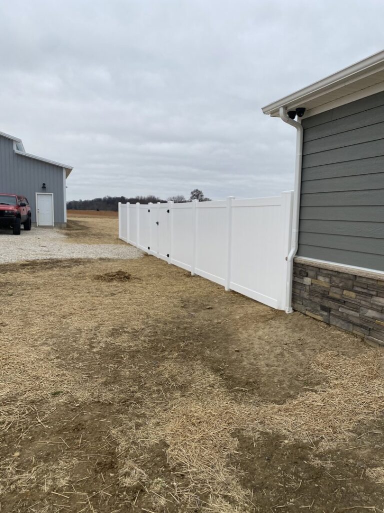A clean white vinyl privacy fence installed alongside a house and barn by Petty Fence Company LLC in Evansville, IN.
