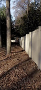 A newly installed white vinyl privacy fence along a property line by Building Fences in Westchester NY.