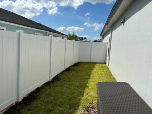 A pristine white vinyl privacy fence installed along a residential side yard by Exacta FENCE LLC, a fencing contractor in Jacksonville, FL.