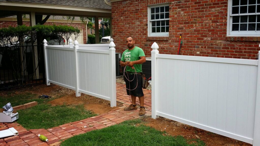 A worker standing by a newly installed white vinyl privacy fence by G L Fence & Remodeling, serving clients in Arlington, TX.
