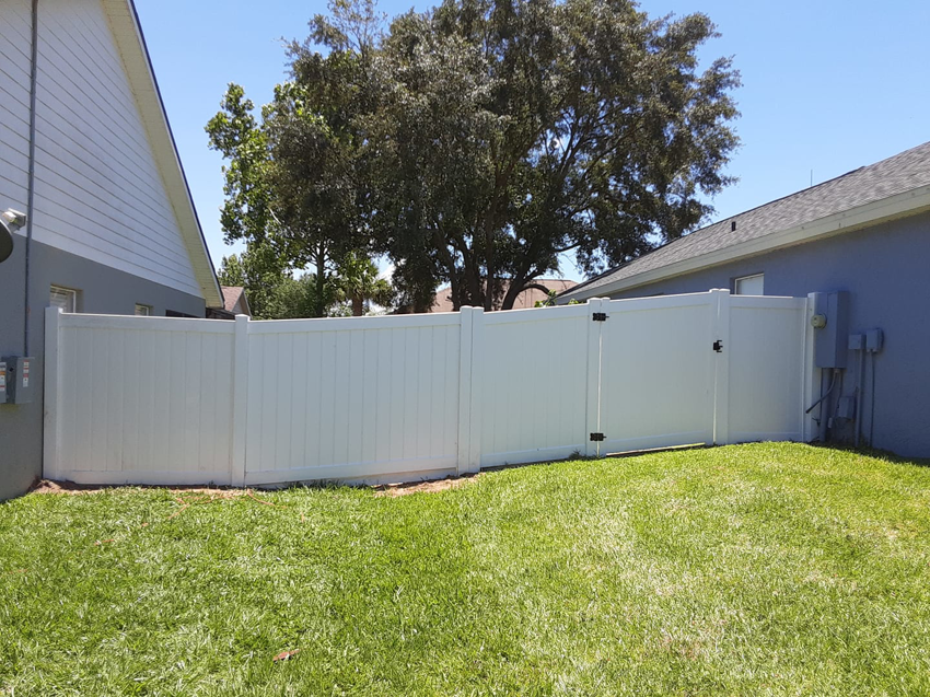 A white vinyl privacy fence with a gate installed between two homes by Goldstar Fencing in Mascotte, FL.