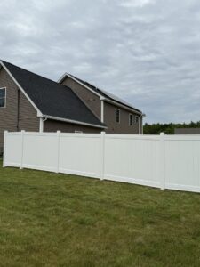 A pristine white vinyl privacy fence installed alongside a modern home by Triple P Fence in Augusta, ME.