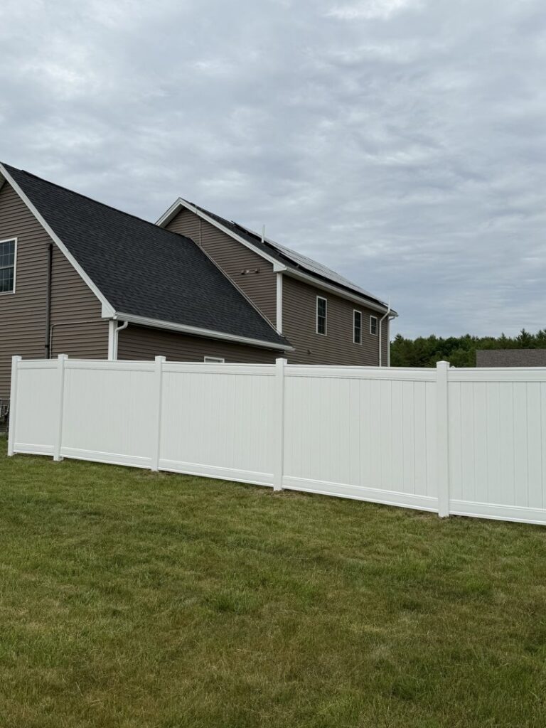 A pristine white vinyl privacy fence installed alongside a modern home by Triple P Fence in Augusta, ME.