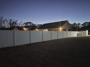 A long white vinyl privacy fence installed in a backyard, illuminated at night by Fayetteville Fence Pros in Fayetteville, NC.