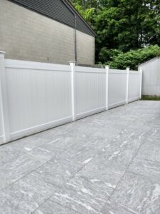 A modern white vinyl privacy fence installed alongside a tiled outdoor patio by New England landscaping and fence inc in Lynn, MA.