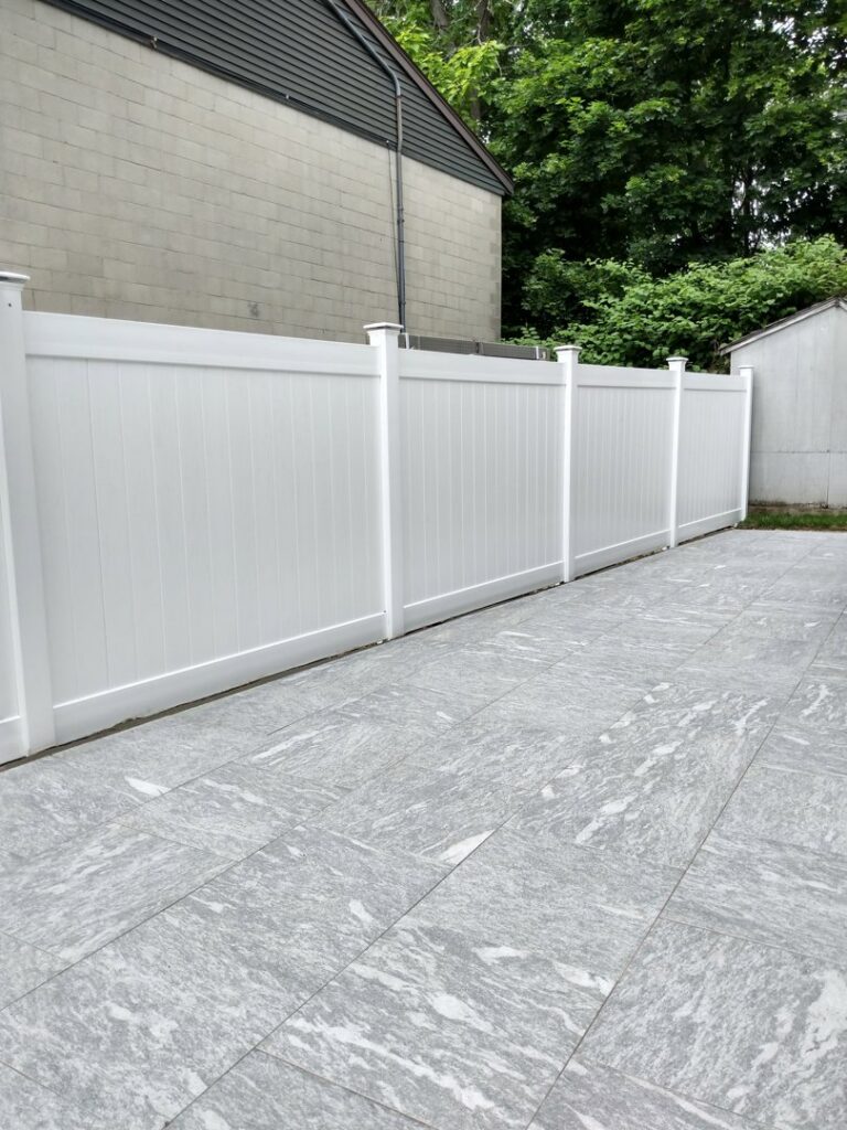 A modern white vinyl privacy fence installed alongside a tiled outdoor patio by New England landscaping and fence inc in Lynn, MA.