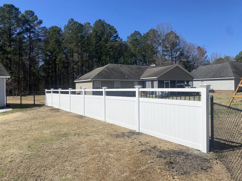 A newly installed white vinyl privacy fence with decorative accents by Renegade Fencing, LLC in Jacksonville, NC.