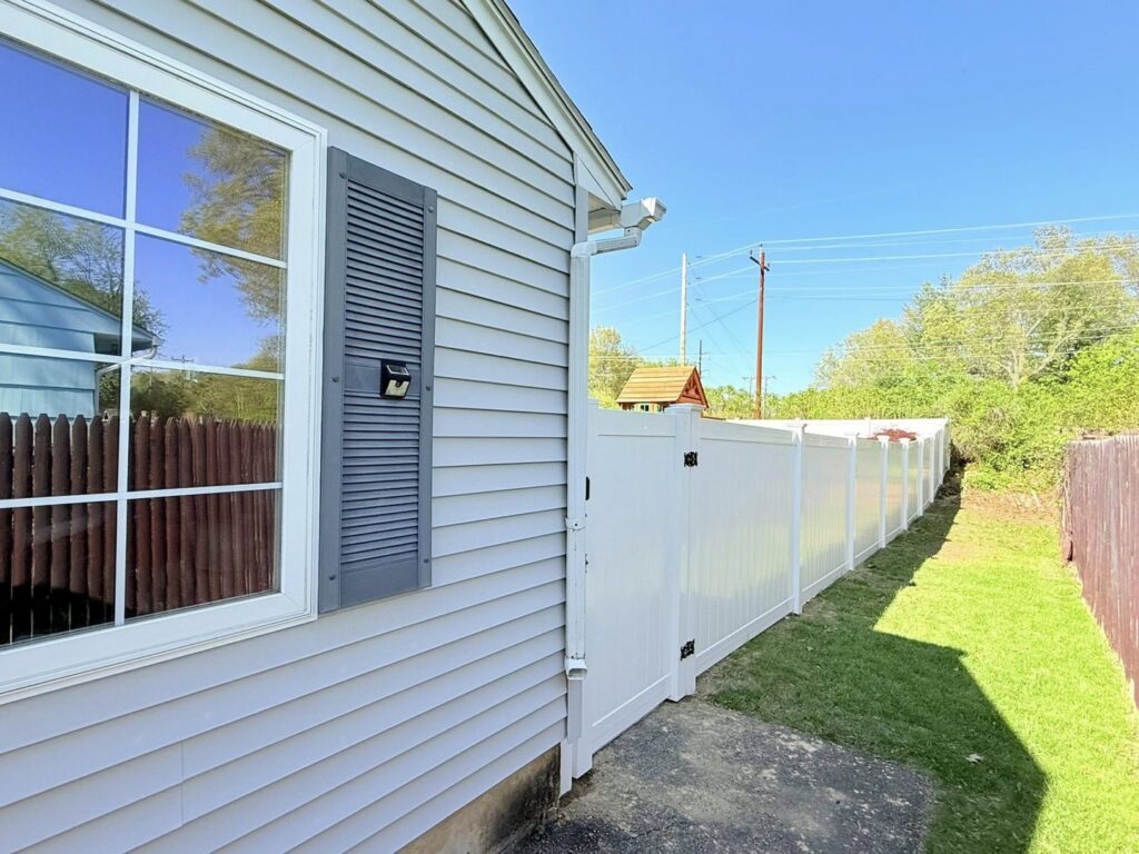 A long white vinyl privacy fence installed alongside a residential property by Ultra Fence LLC in Brookline, NH.