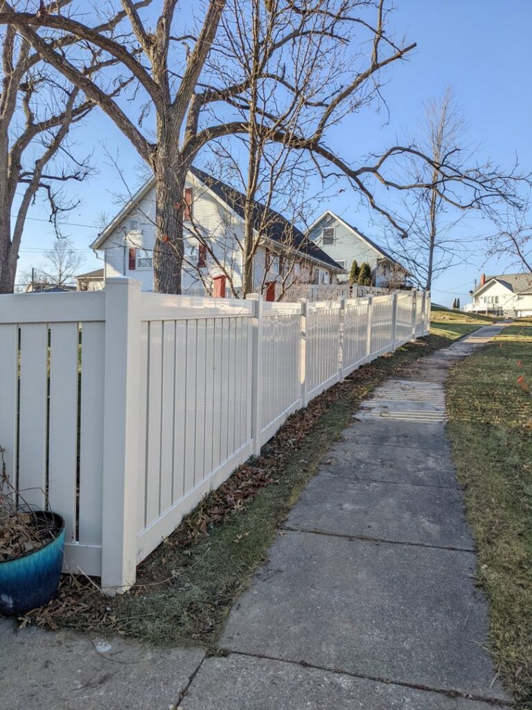 A newly installed white vinyl privacy fence along a residential sidewalk by Corridor Residential Fencing Co. in Cedar Rapids, IA.