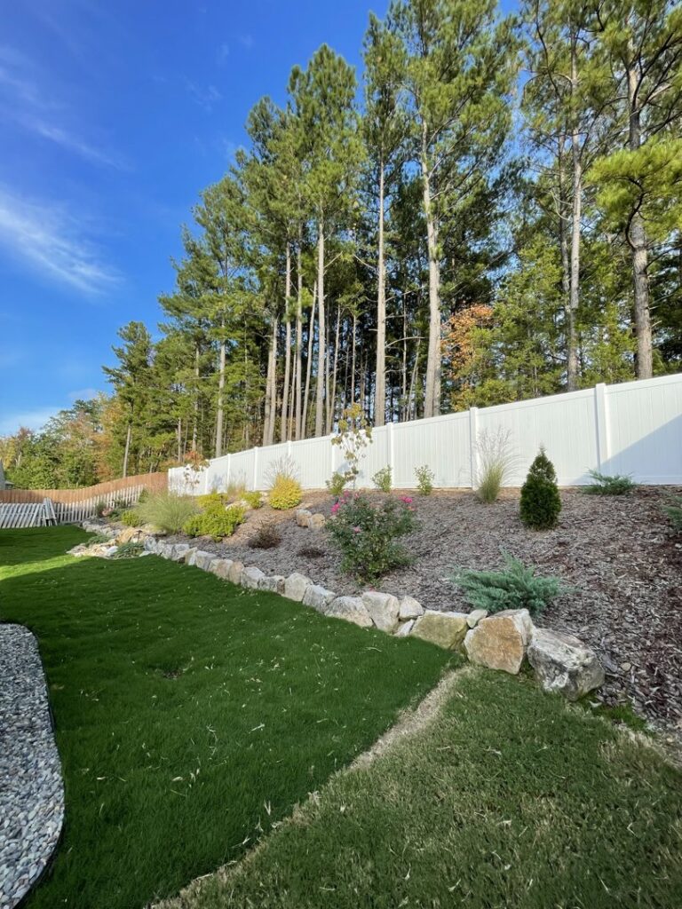 A white vinyl privacy fence installed on a sloped backyard landscape by Align Fence Builders in Durham, NC.