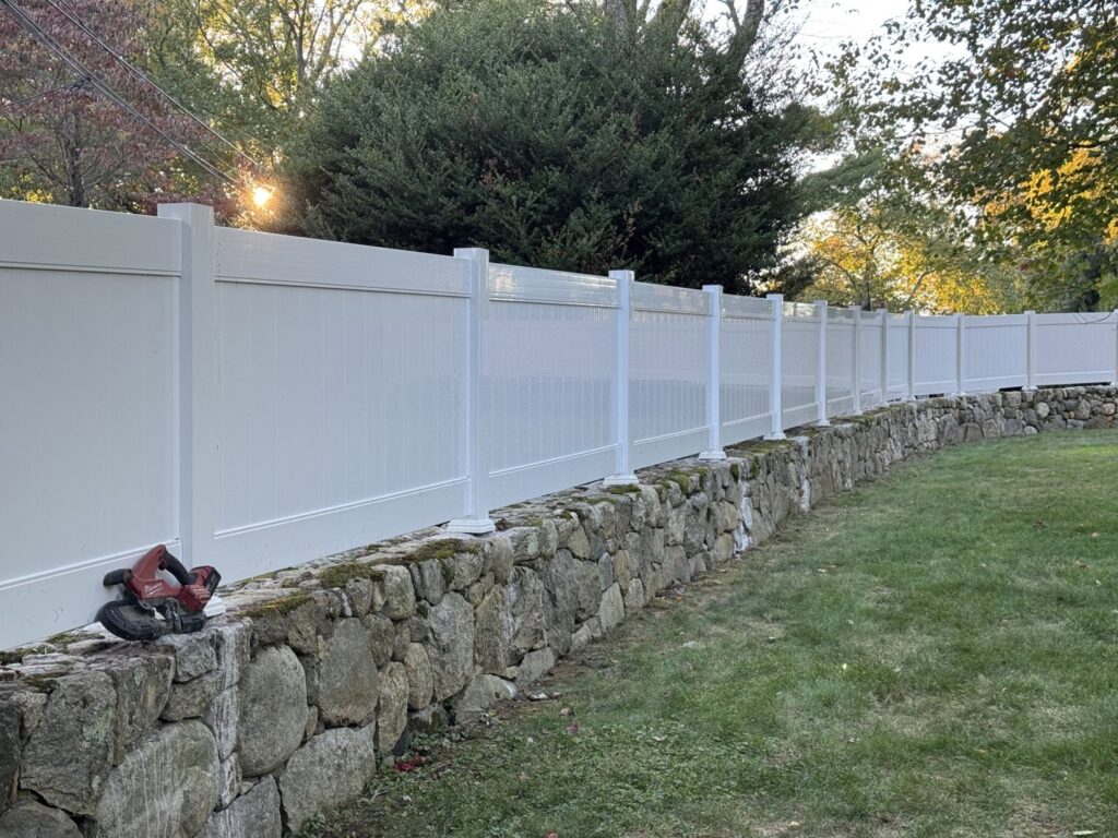 A clean white vinyl privacy fence installed on a stone wall by Flanagan Fencing in Brookfield, CT.