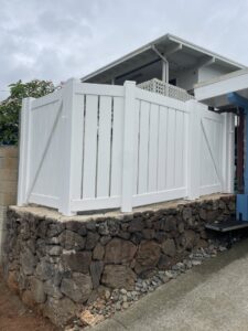 A white vinyl privacy fence with a gate installed on a stone retaining wall by Redmond Valleywide - Hawaii's Fence Company in Kapolei, HI
