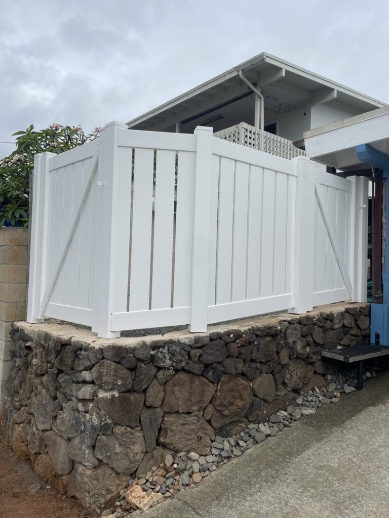 A white vinyl privacy fence with a gate installed on a stone retaining wall by Redmond Valleywide - Hawaii's Fence Company in Kapolei, HI