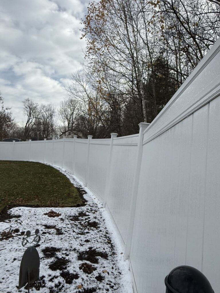 A long white vinyl privacy fence installed in a backyard with patches of snow by Triple P Fence in Augusta, ME.