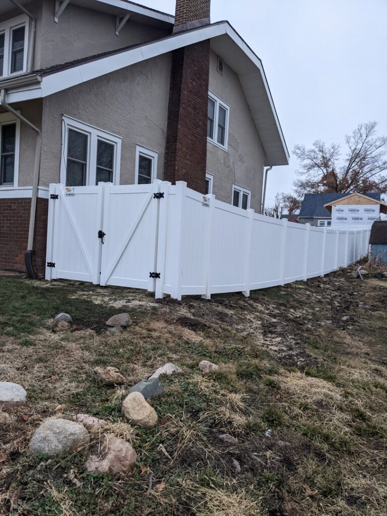 A newly installed white vinyl privacy fence with a gate next to a residential house by Corridor Residential Fencing Co. in Cedar Rapids, IA.